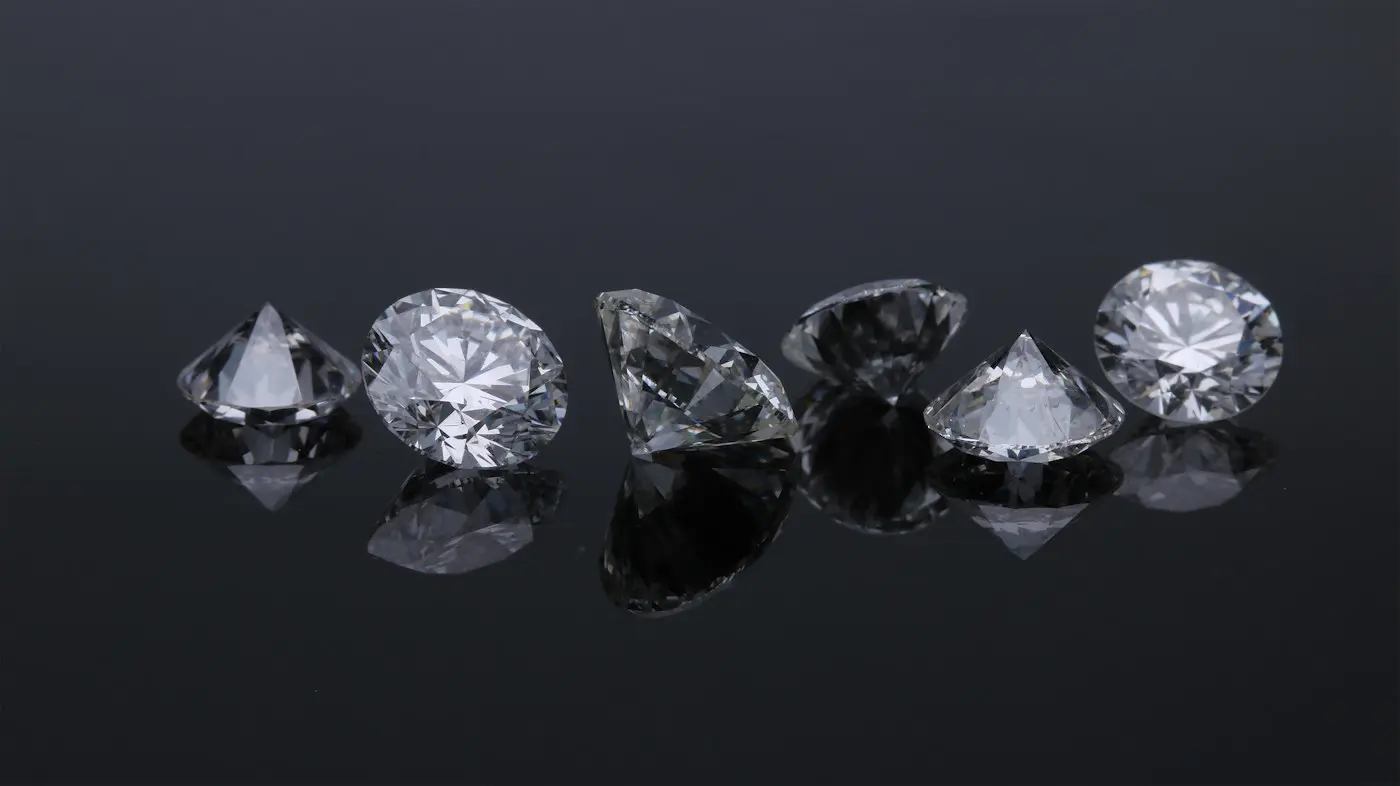 Six faceted diamonds arranged in a row on a reflective black surface