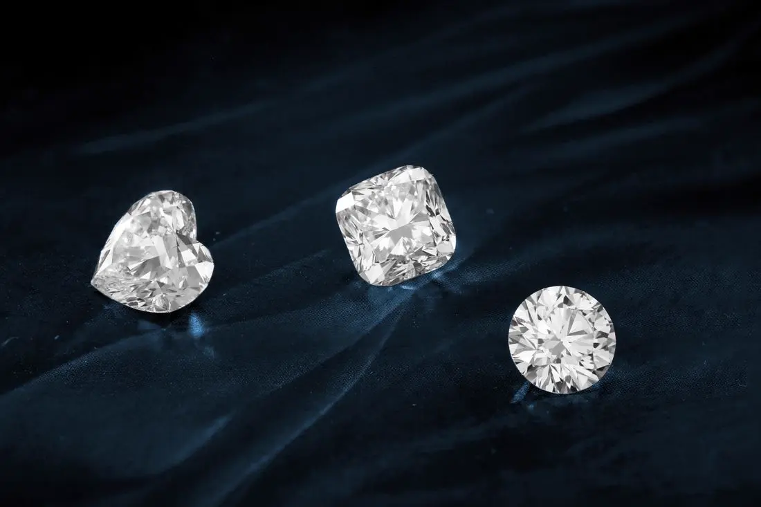 Three diamonds in heart, cushion and round cuts on a dark surface