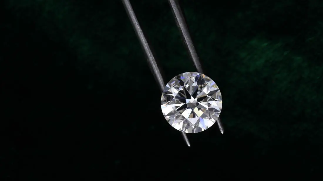 A round diamond held in tweezers against a dark textured background